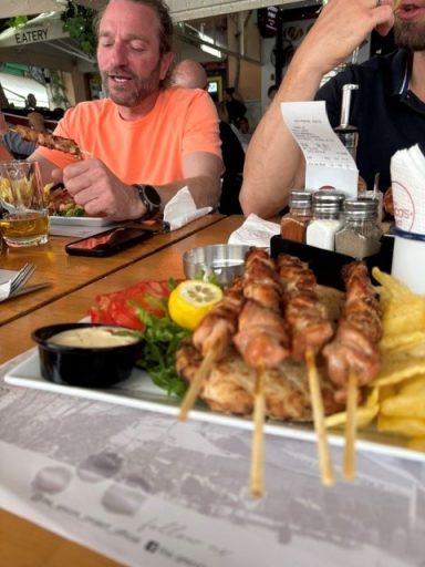 Kipsate met friet, salade en saus, met mensen aan tafel op de achtergrond.