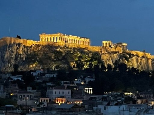 De Akropolis verlicht boven een stad, tegen een schemerige blauwe lucht.